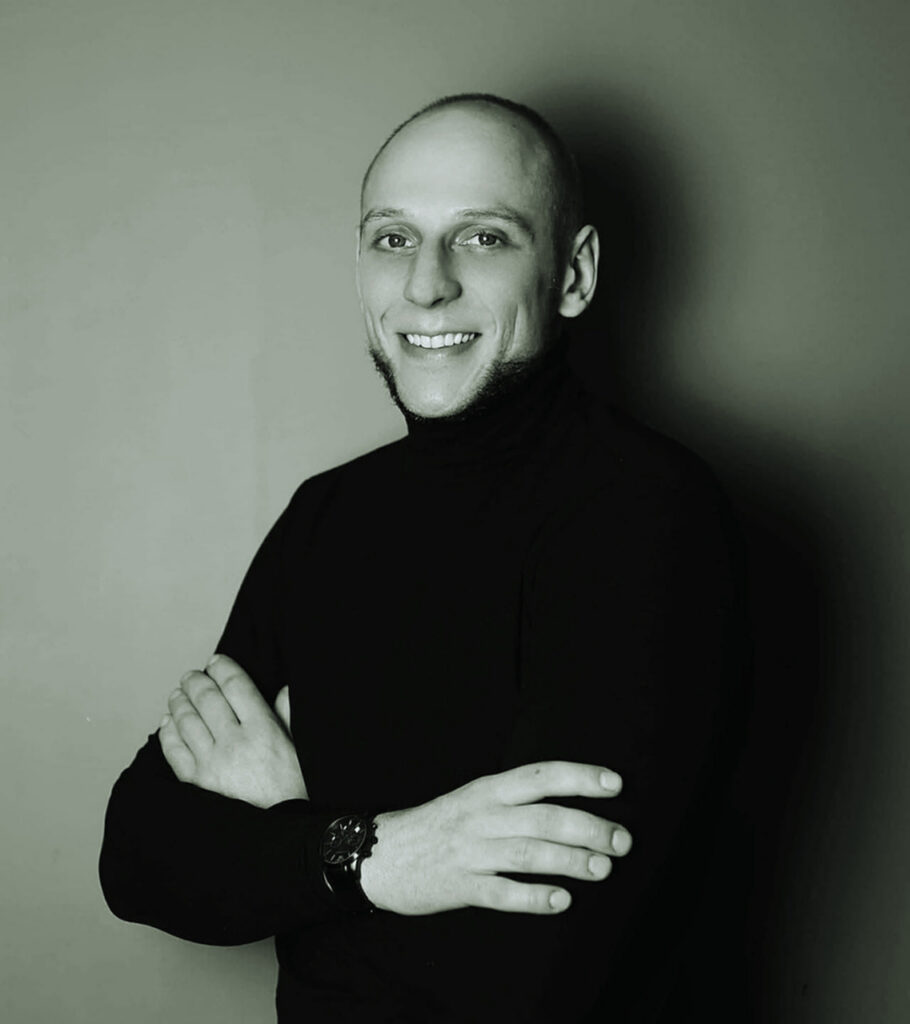 Młody , dobrze zbudowany mężczyzna w czarnym golfie, skrzyżowane ręce na piersiach